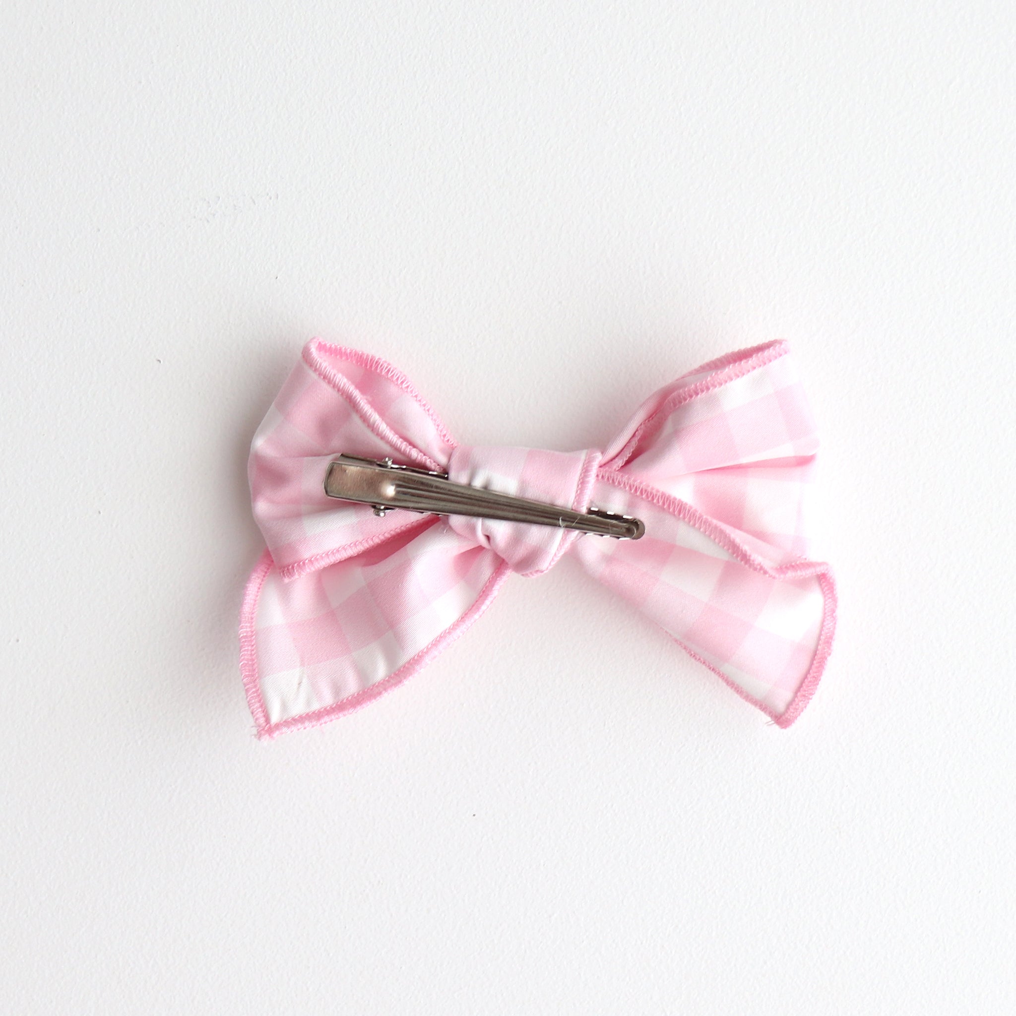 Pink bow hair clip on a white background showing back of the bow with the clip