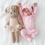 Baby in pink checkered outfit with teddy bear toy on white background