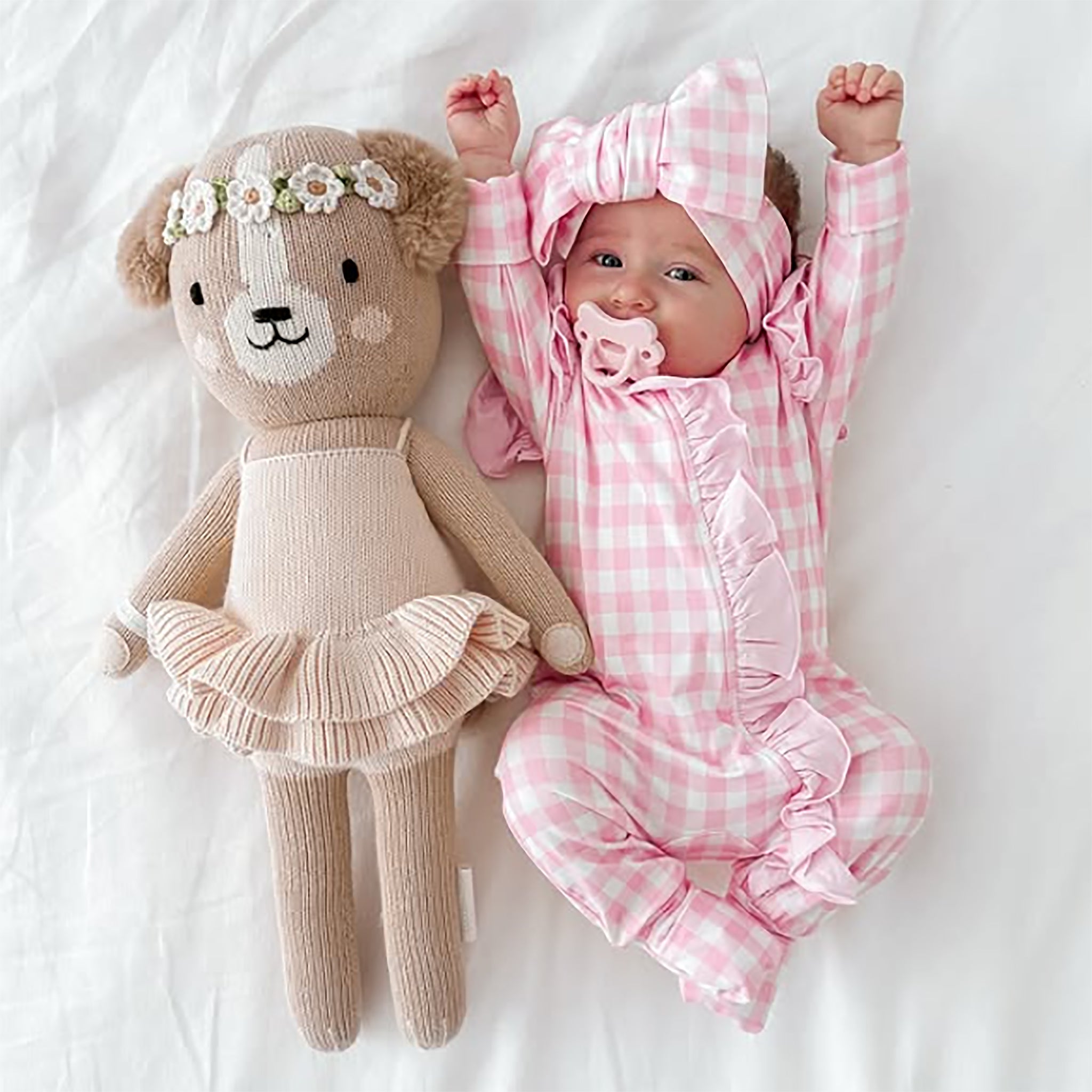 Baby in pink checkered outfit with teddy bear toy on white background