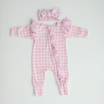 A pink gingham frilly onesie with long sleeves and a matching gingham bow, laid flat on a white background.