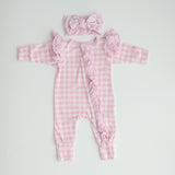A pink gingham frilly onesie with long sleeves and a matching gingham bow, laid flat on a white background.