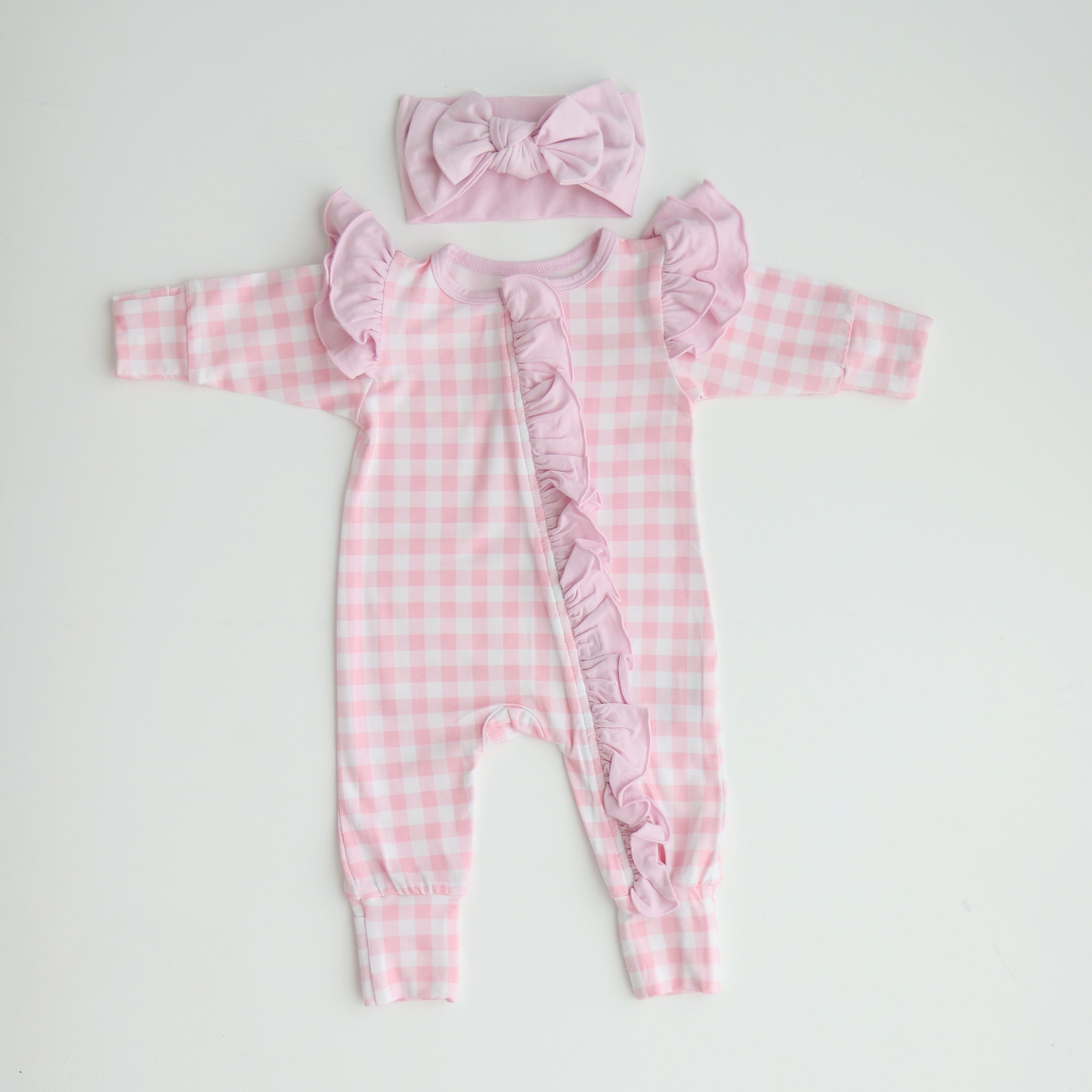 A pink gingham frilly onesie with long sleeves and a matching gingham bow, laid flat on a white background.