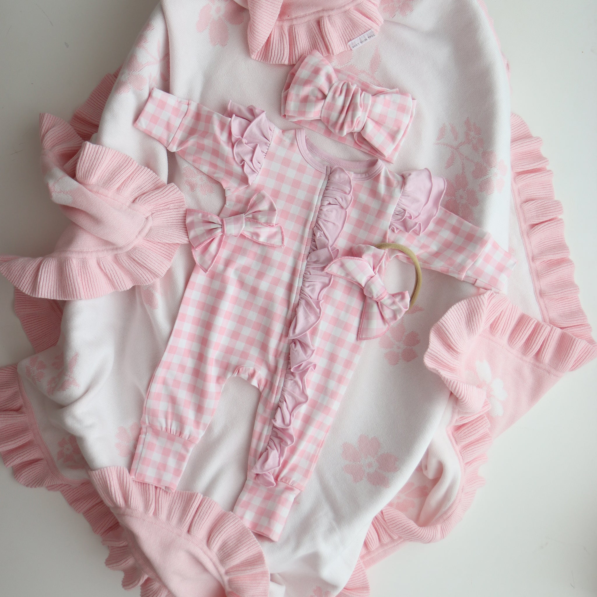 Pink and white checkered baby outfit with ruffles on a light background