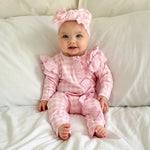 baby dressed in pink gingham frilly onesie with matching one size bow sitting on white blanket