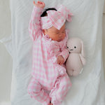 aby in pink checkered outfit with matching hat and bunny toy on white blanket
