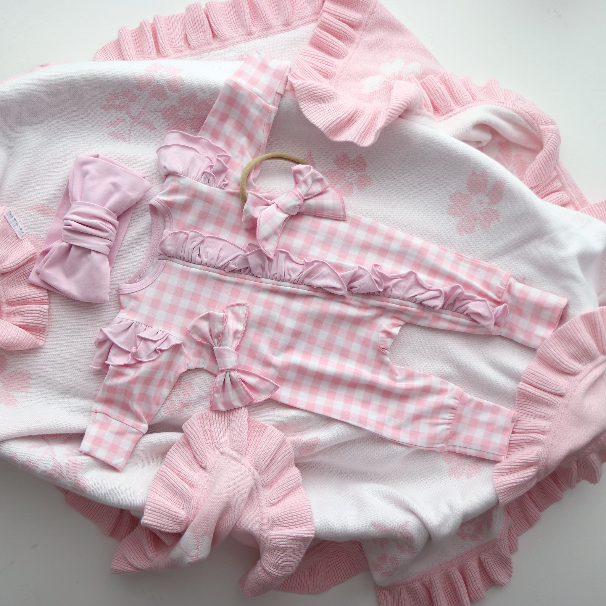 Pink and white baby outfit with ruffles and checkered patterns on a white background