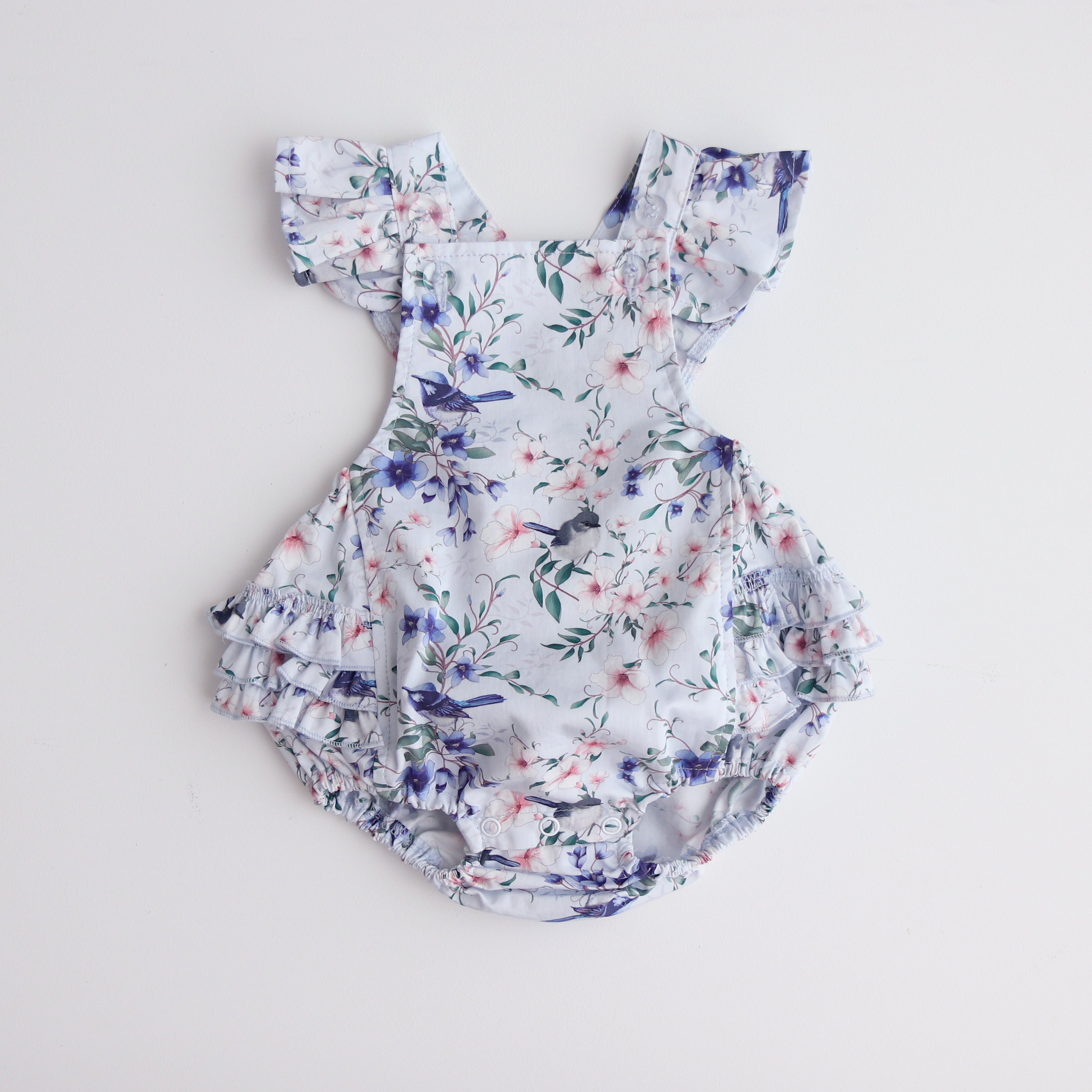 playsuit with frill on shoulders,crossover straps, frill on the lower bottom and snaps  at crotch for easy changing. Flatlay showing the playsuiton white back ground