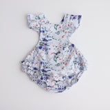 playsuit with frill on shoulders,crossover straps, frill on the lower bottom and snaps  at crotch for easy changing. Flatlay showing the playsuiton white back ground