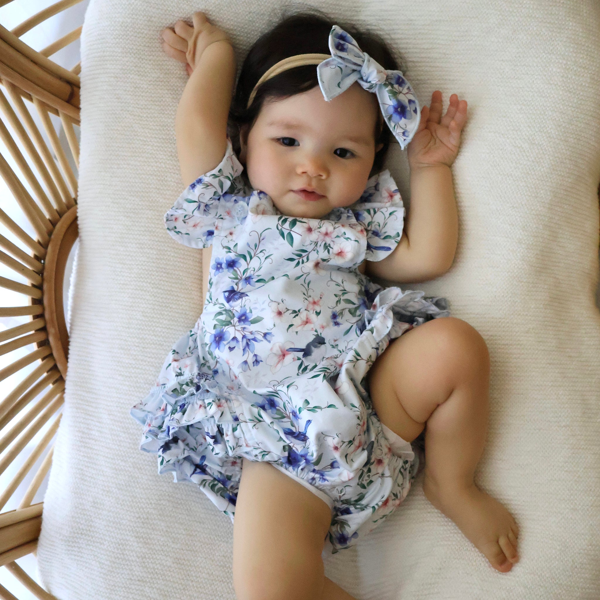 Baby wearing a floral romper and headband lying on a white cushion