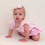 Baby in a pink outfit with a bow sitting on a white surface