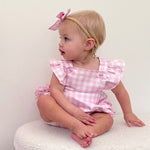 Baby wearing a pink checkered outfit with ruffled sleeves and a bow headband.