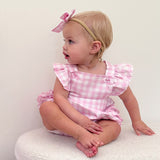 Baby wearing a pink checkered outfit with ruffled sleeves and a bow headband.