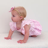 Baby in a pink checkered outfit crawling on a white surface