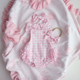 Pink checkered baby romper with ruffles on a white blanket