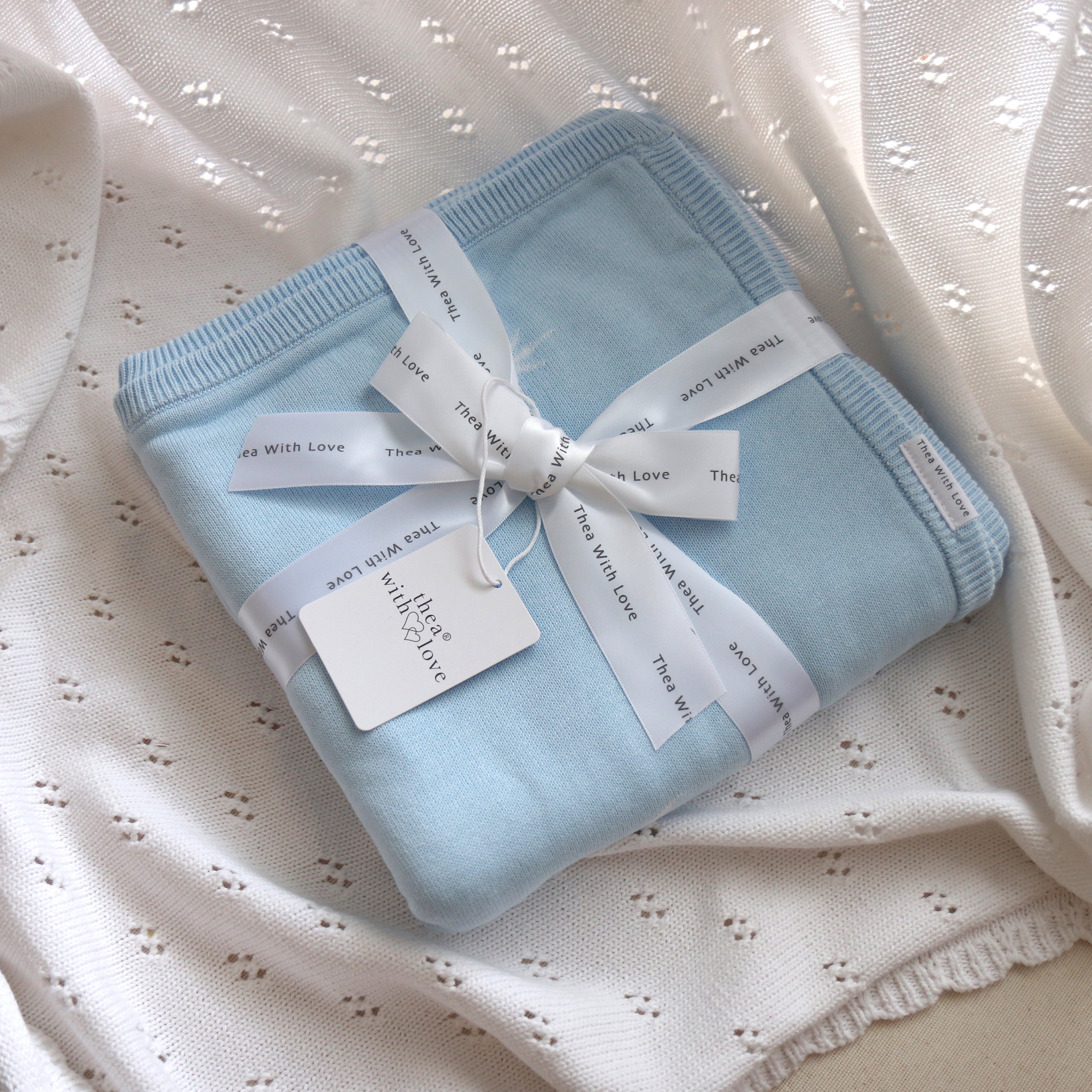 Baby blue cotton knit blanket with stars and moon pattern by Thea With Love, folded neatly on white background.