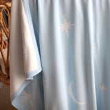 Light blue curtain with star and moon patterns draped over a cane bassinet.