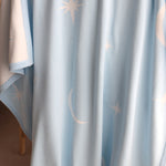 Baby blue blanket with star and moon patterns draped over cane bassinet.

