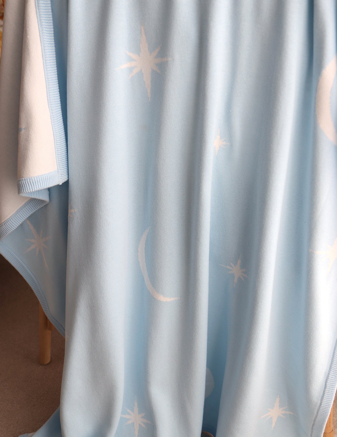 Baby blue blanket with star and moon patterns draped over cane bassinet.

