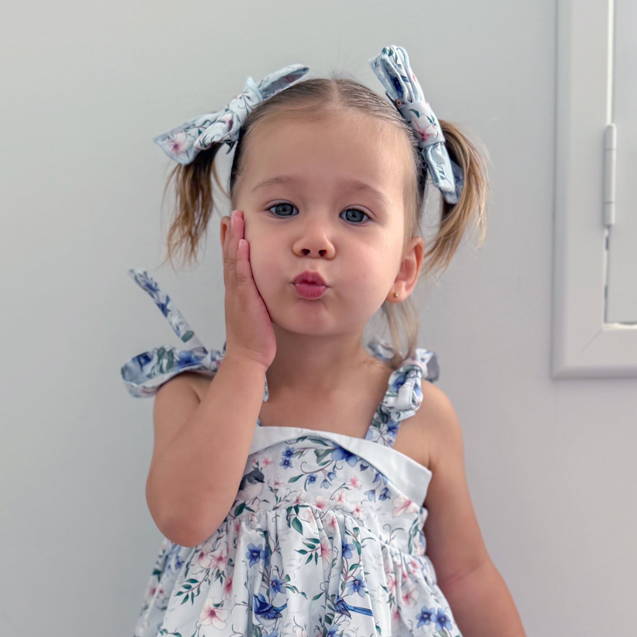 Young girl wearing a floral dress and headbands against a plain background