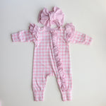 Pink checkered baby romper with ruffles and matching headband on a light gray background