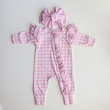 Pink checkered baby romper with ruffles and matching headband on a light gray background