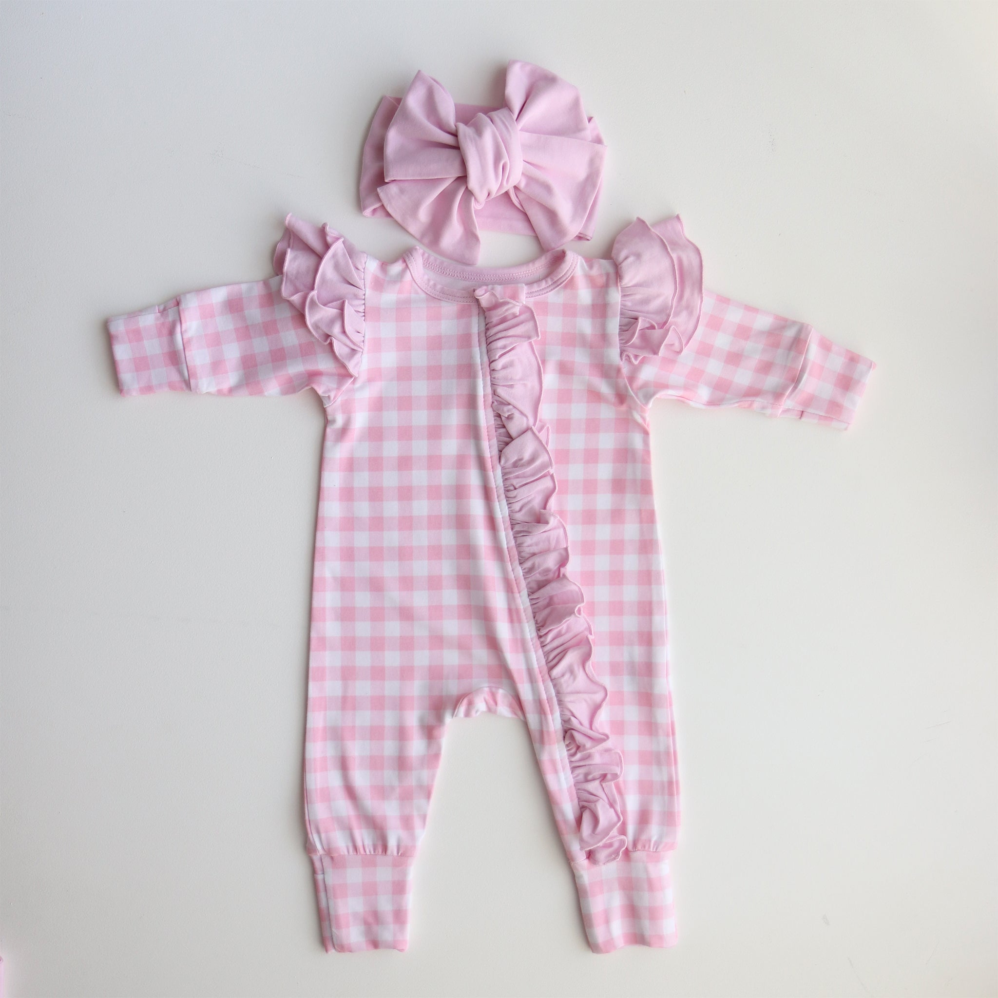 Pink checkered baby romper with ruffles and matching headband on a light gray background