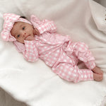 baby dressed in pink gingham frilly onesie with matching one size bow laying on white blanket