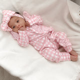 baby dressed in pink gingham frilly onesie with matching one size bow laying on white blanket