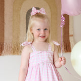 Young girl in a pink dress with a bow in her hair, holding a pink wand and balloon.