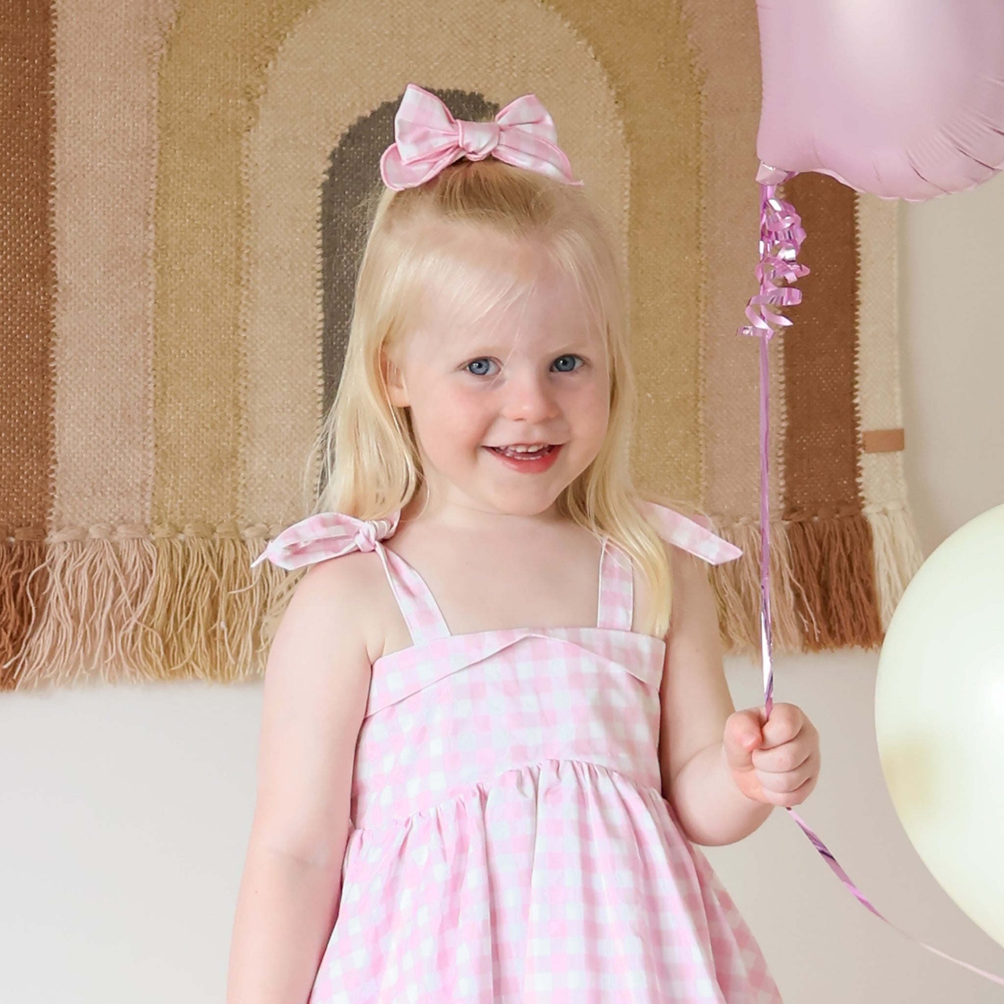 Young girl in a pink dress with a bow in her hair, holding a pink wand and balloon.