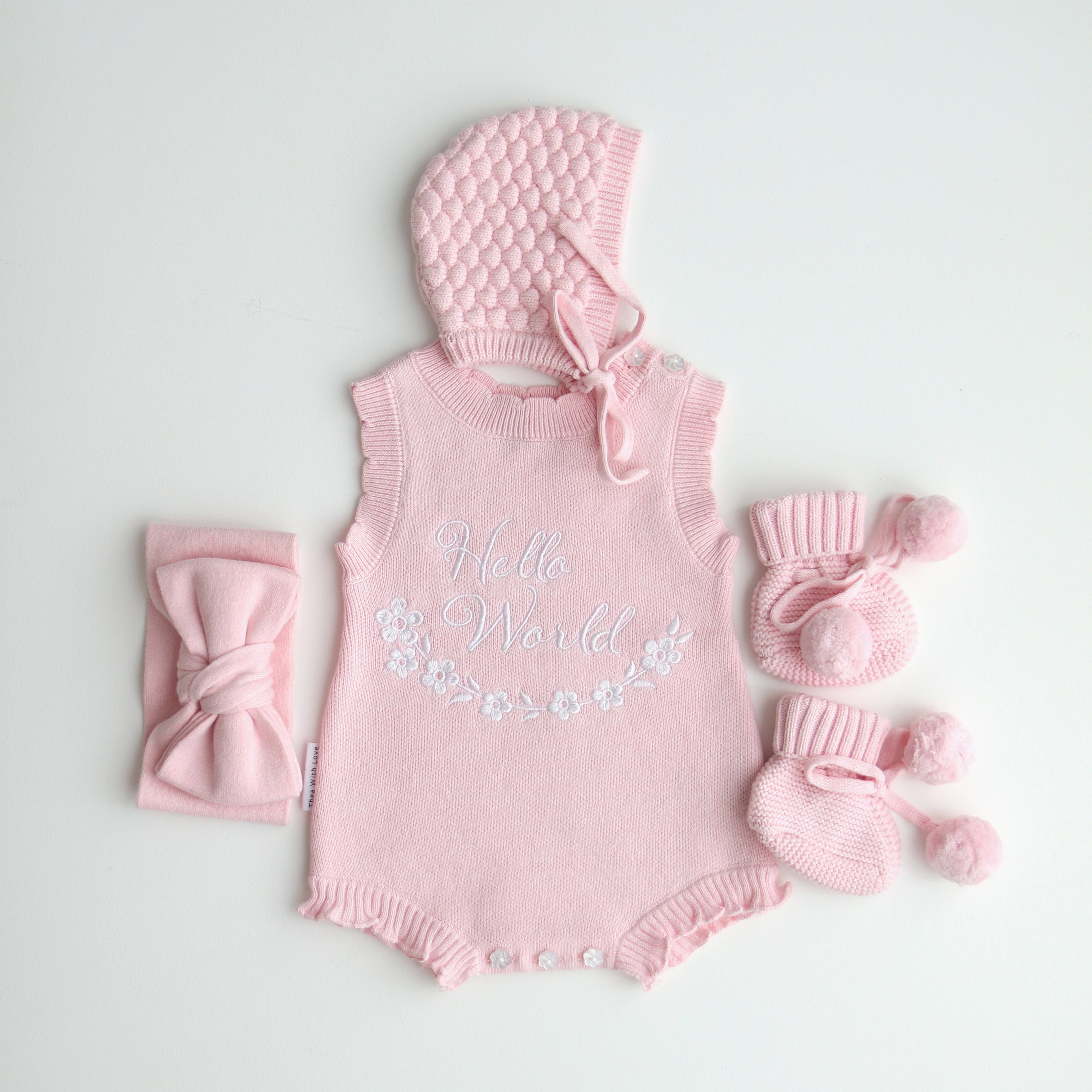 our pretty pink hello world has scalloped edges on short sleeve for arms and delicate knitted frill on legs. At the crotch and down the centre and on shoulder we have added pink resin flower buttons. Matches with our bonnet booties beanie and other pretty pink items. Hello world type in the centre is white surrounded by delicate flowers. The type is in running writing with capital letters at the start - beautiful for baby girl 