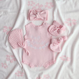 our pretty pink hello world has scalloped edges on short sleeve for arms and delicate knitted frill on legs. At the crotch and down the centre and on shoulder we have added pink resin flower buttons. Matches with our bonnet booties beanie and other pretty pink items. Hello world type in the centre is white surrounded by delicate flowers. The type is in running writing with capital letters at the start - beautiful for baby girl 