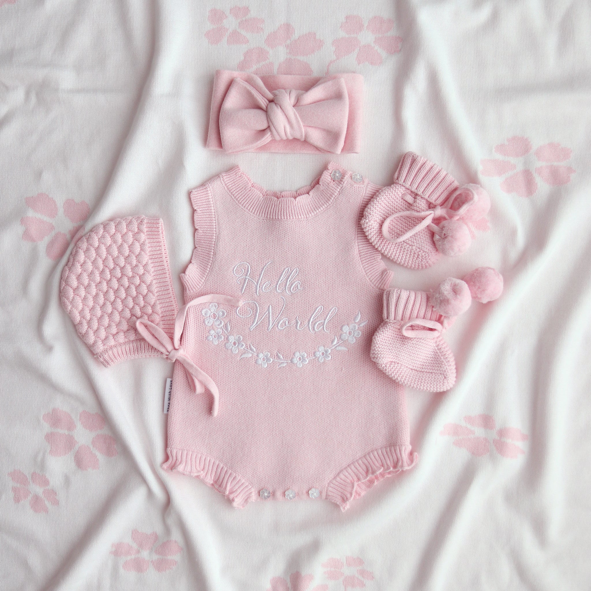 our pretty pink hello world has scalloped edges on short sleeve for arms and delicate knitted frill on legs. At the crotch and down the centre and on shoulder we have added pink resin flower buttons. Matches with our bonnet booties beanie and other pretty pink items. Hello world type in the centre is white surrounded by delicate flowers. The type is in running writing with capital letters at the start - beautiful for baby girl 