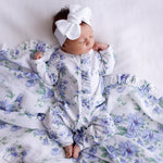 newborn hibiscus frill onesie. certified organic cotton with hibiscus blue flower print with white bow for headwear on baby laying on hibiscus frill muslin swaddle